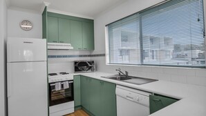 A compact kitchen with white and green cabinetry, a built-in oven, a microwave, and a sink.