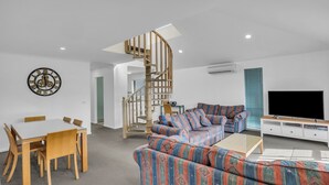 A modern living room with a spiral staircase, a sofa set, a dining table with chairs, and a flat-screen TV.