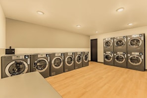 A laundry room with multiple washing machines, wooden flooring, and recessed ceiling lights. - LivAway Suites Portland-Scarborough (Scarborough)