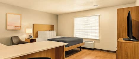 Una habitación de hotel pequeña con cama, escritorio, silla y televisor sobre un mueble de madera.