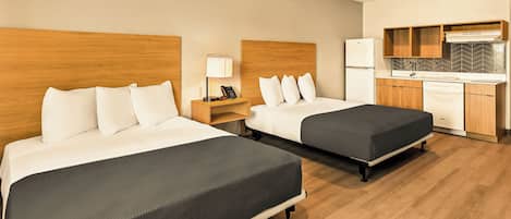 A hotel room with two beds, a kitchenette, and a wooden floor.