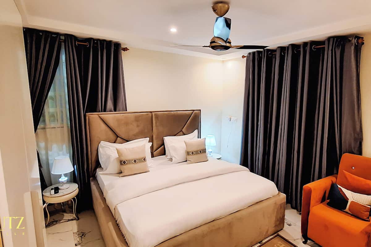 Une chambre d’hôtel avec un lit, un fauteuil orange, un ventilateur de plafond et un appareil de climatisation.