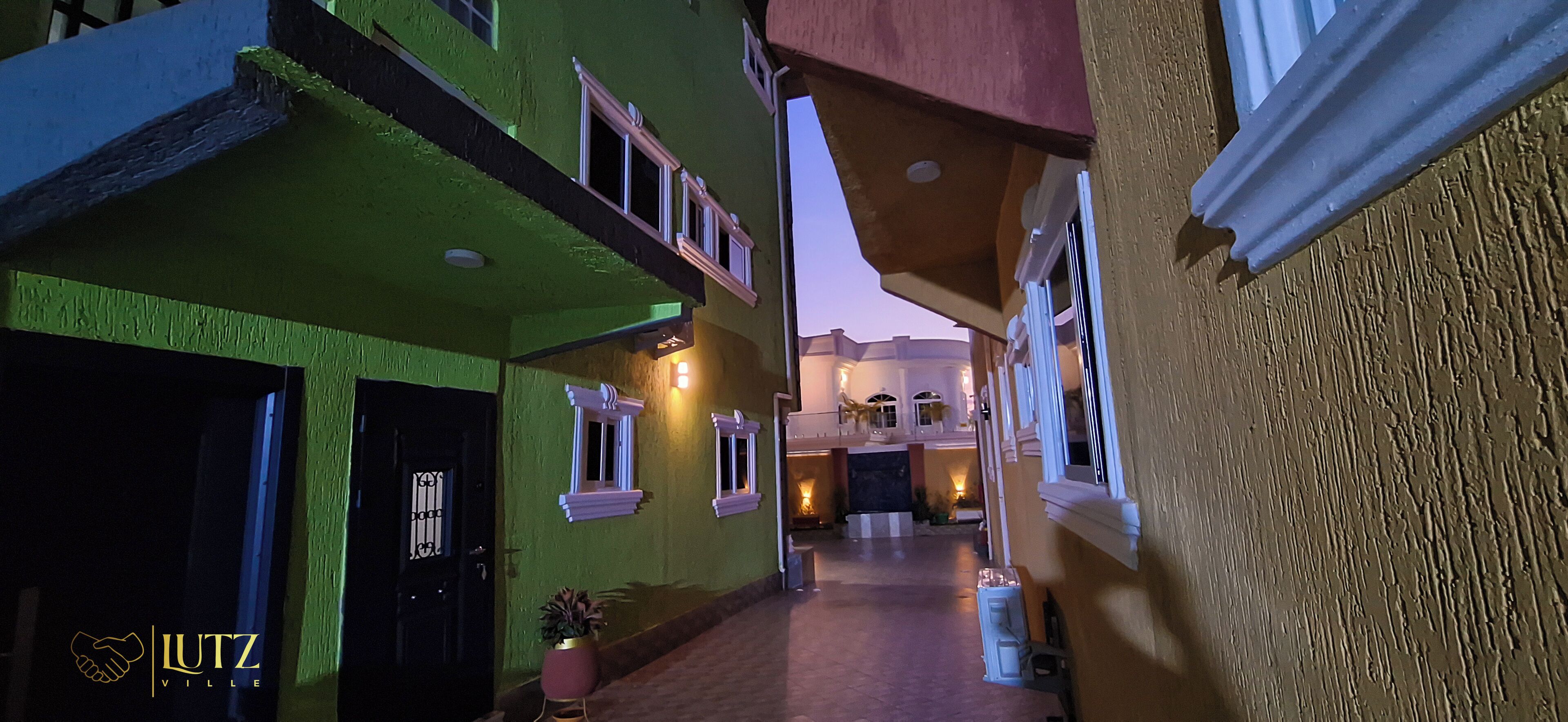 Un estrecho callejón con edificios pintados de verde y amarillo, que conduce a un edificio con balcón y entrada iluminada.