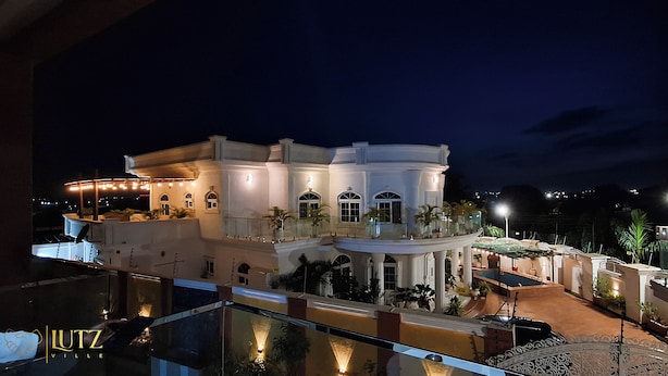 A large, multi-story building with a balcony and outdoor seating area, surrounded by palm trees and well-lit at night. - Lutz Ville Apartments (Kumasi)