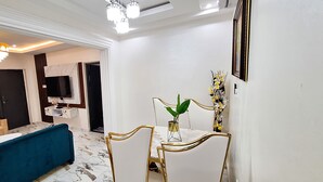 Un salon moderne avec un canap é bleu, une table à manger avec des chaises, un téléviseur fixé au mur et une plante décorative.