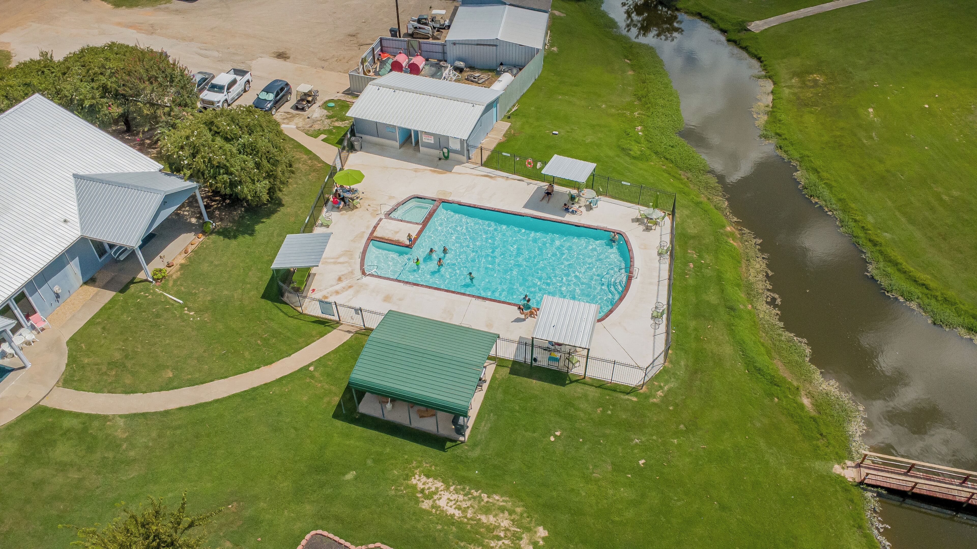 An aerial view of a residential area with a swimming pool, a small boat dock, and a river.
