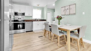 Una cocina moderna con electrodomésticos de acero inoxidable, una mesa de comedor con sillas y una pared verde claro con un letrero que dice 'gather'.