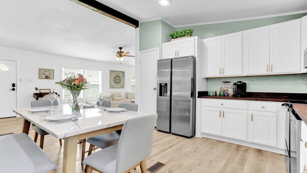 Una cocina moderna con armarios blancos, electrodomésticos de acero inoxidable y una zona de comedor con una mesa blanca y sillas grises.