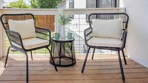 Una terraza de madera con dos sillas de mimbre y una mesita con un florero y dos tazas.