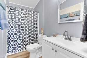Ein Badezimmer mit gemustertem Duschvorhang, einer weißen Toilette, einem Waschbecken mit Spiegel und einem Handtuch an der Wand.