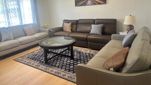 A living room with a brown leather sofa, a glass coffee table, and a patterned rug. - Charming Vacation Home Near Niagara Falls & Highmark Stadium (Depew)