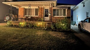 A two-story house with a covered porch, a brick facade, and a white car parked in the driveway. - Charming Vacation Home Near Niagara Falls & Highmark Stadium (Depew)