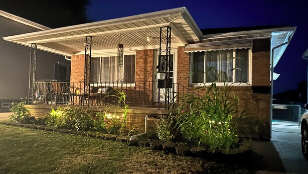A modern house with a covered porch, brick exterior, and a well-lit garden area. - Charming Vacation Home Near Niagara Falls & Highmark Stadium (Depew)
