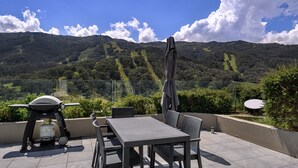 A patio with a grill, table, chairs, and an umbrella.