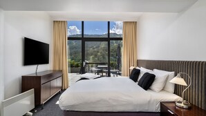 A hotel room with a large bed, a TV, a desk, and a view of a mountainous landscape.