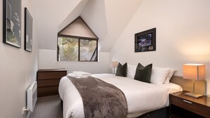 Un dormitorio con cama, mesitas de noche, una ventana y un cuadro en la pared.