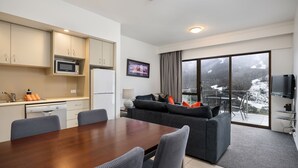A modern hotel room with a dining area, kitchenette, and a balcony with a scenic view. - Lantern 24 Balcony (Thredbo)