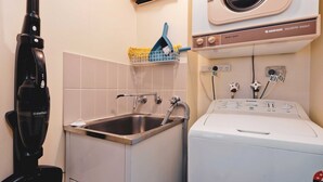 A laundry area with a washing machine, a sink, and a vacuum cleaner. - Lantern 24 Balcony (Thredbo)