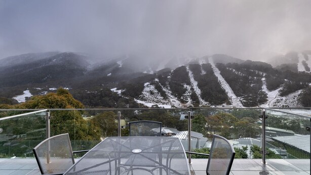 A table and chairs on a balcony overlooking snow-covered mountains and a valley. - Lantern 24 Balcony (Thredbo)