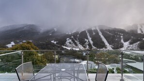 Een tafel met stoelen op een balkon met uitzicht op besneeuwde bergen en een vallei.