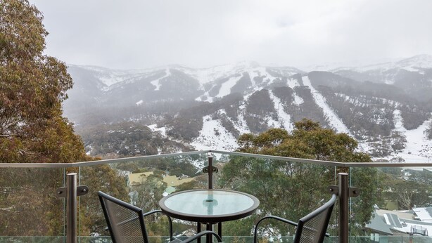 A balcony with a table and chairs overlooking a mountainous landscape with snow. - Lantern 19 Deluxe (Thredbo)