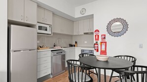 A modern kitchen with stainless steel appliances, a dining table with chairs, and a decorative mirror. - Lantern 19 Deluxe (Thredbo)