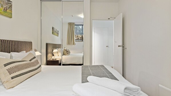 A hotel room with a bed, a nightstand, a lamp, a window with curtains, and a door.