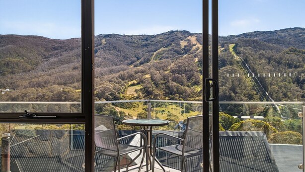 A balcony with a table and chairs, offering a view of a mountainous landscape. - Lantern 12 Balcony - views from every window (Thredbo)