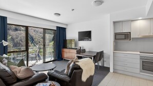 A modern living room with a sofa, coffee table, and a dining area with a TV. - Lantern 12 Balcony - views from every window (Thredbo)
