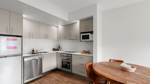 A modern kitchen with stainless steel appliances, white cabinetry, and a wooden dining table with chairs.