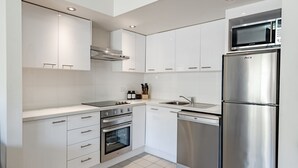 A modern kitchen with white cabinetry, a built-in oven, a dishwasher, a microwave, and a stainless steel refrigerator. - Lantern 08 Balcony (Thredbo)