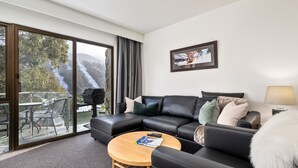Un salon moderne avec un canapé en cuir, une table basse ronde en bois et un balcon offrant une vue sur un paysage montagneux.