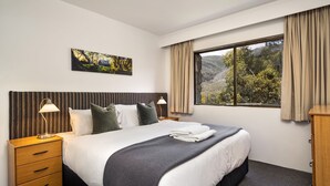 Une chambre d’hôtel avec un lit, une table de chevet, une lampe, un tableau et une fenêtre avec des rideaux.