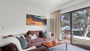 Ein modernes Wohnzimmer mit einer Couch, einem Couchtisch und einem großen Fenster mit Blick auf eine verschneite Landschaft.