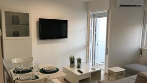 A modern living room with a dining area, a flat-screen TV, and a sliding glass door leading to a balcony.