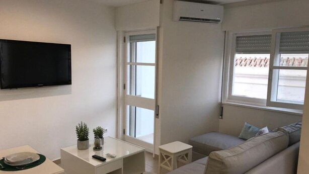 A modern living room with a flat-screen TV, a sofa, a small table, and a window with blinds.