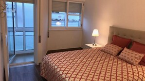A bedroom with a bed, a nightstand, a lamp, and a window with blinds.