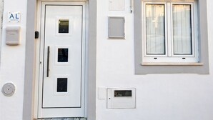 A white building with a door, three windows, and a small sign with 'AL' on it.