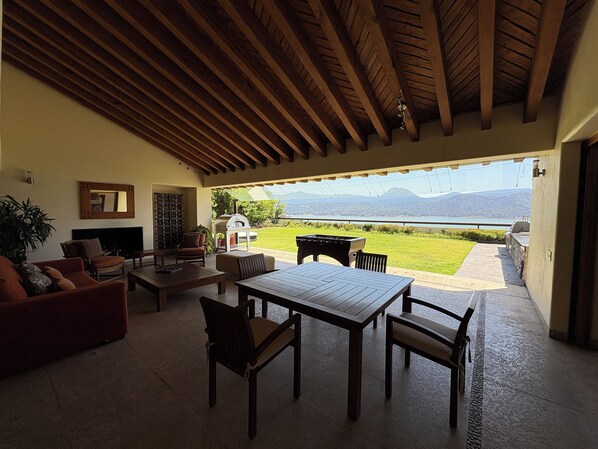 An outdoor patio with a wooden ceiling, a fireplace, a table, and chairs.