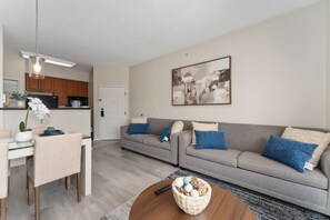 Un salon moderne avec un canapé gris, une table à manger avec des chaises, une table basse agrémentée d’objets décoratifs et, au fond, une cuisine.