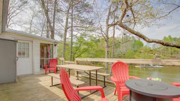 A deck with red chairs, a table, and a view of a lake.