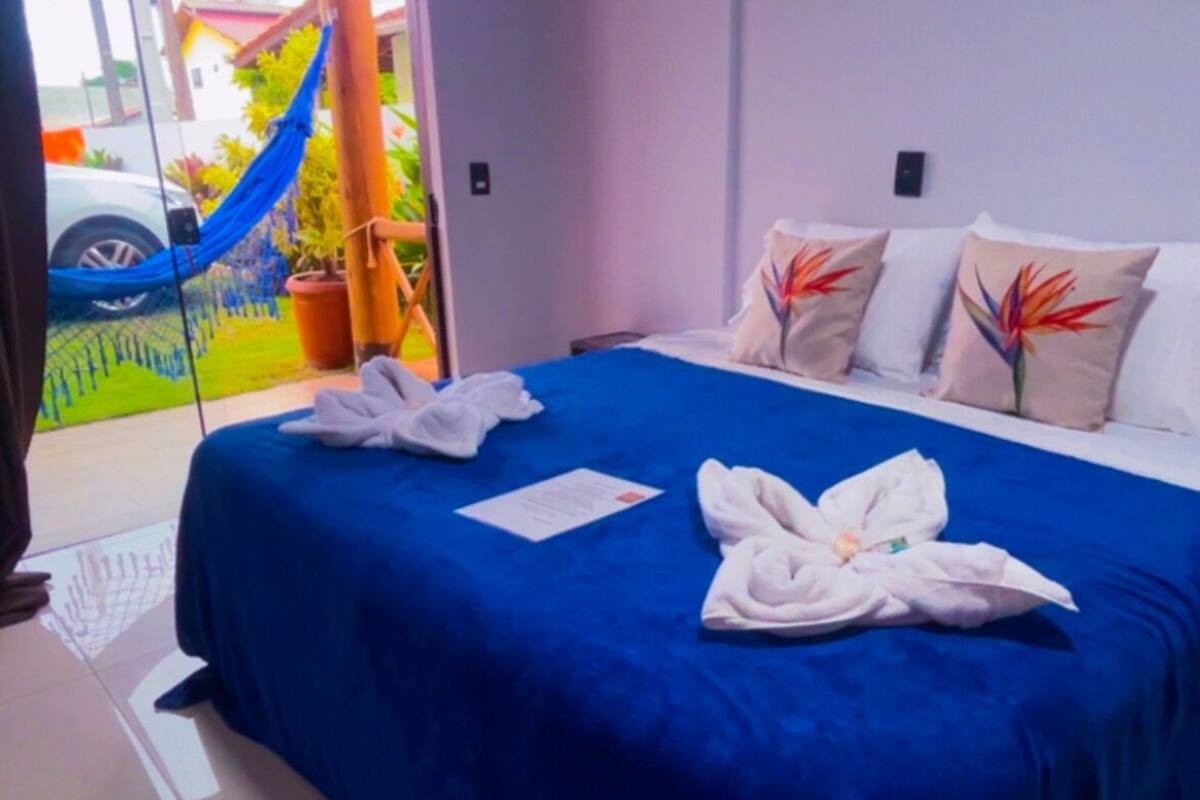 A hotel room with a large bed, a blue bedspread, and a view of the outside.