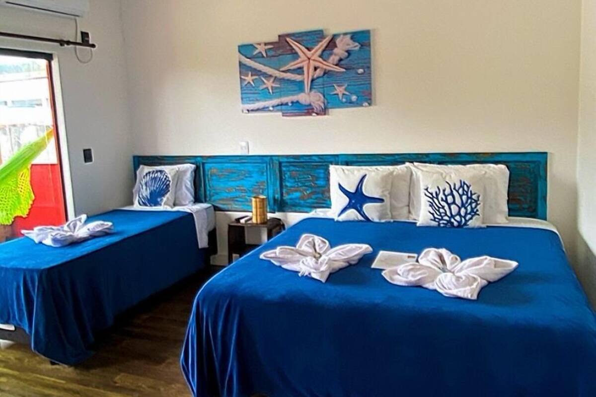 A hotel room with two beds, each with blue bedding and starfish pillows, a painting of a starfish on the wall, and a wooden floor.