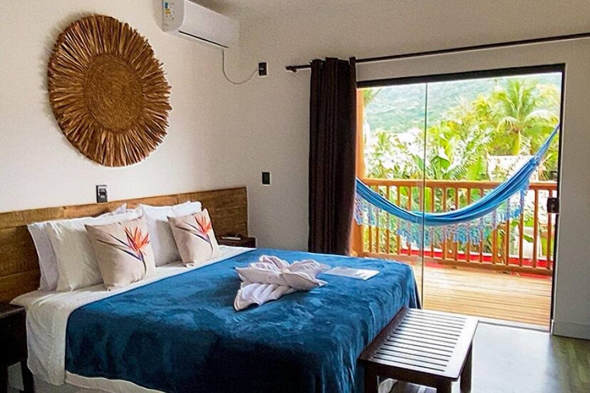 A bedroom with a bed, a bench, a wall-mounted air conditioner, a woven wall decoration, and a view of a balcony with a hammock.