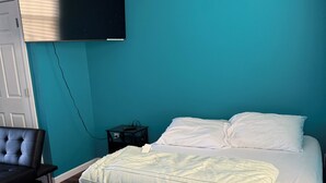 Ett sovrum med en säng, en stol, en tv som är monterad på väggen och ett trägolv.