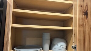 Ett träskåp med tre hyllor, där varje hylla innehåller en stapel tallrikar och en cylindrisk behållare.