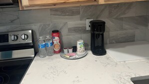 Ett kök med en spis, vattenflaskor, en kaffebryggare och en tallrik med tepåsar.