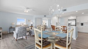 A spacious living room with a glass-top dining table surrounded by chairs, a chandelier, and a view of the outside. - Oceanwalk 1-605 (New Smyrna Beach)