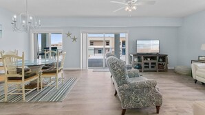 A spacious living room with a glass dining table, patterned sofa, and a ceiling fan. - Oceanwalk 1-605 (New Smyrna Beach)