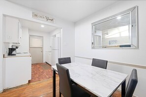 A small, clean room with a dining table, chairs, a kitchen area with a refrigerator, and a mirror on the wall. - Stylish 1 BR Near Deep Ellum (Dallas)